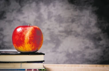 Elämänkatsomustieto 40 vuotta – syrjintää ja saavutuksia. Kuvassa iso punakeltainen omena pöydällä lepäävän kolmen kirjan päällä. Taustana harmaa pilvikuvio.