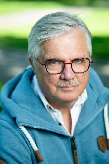 Juha Hänninen pukeutuneena pastellinsiniseen huppariin. Taustalla aurinkoinen nurmikko.