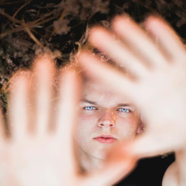 Lapsi katsoo kiinteästi kohti kameraa eteen ojennettujen kämmenten takaa. Peter Kokhanets / Unsplash