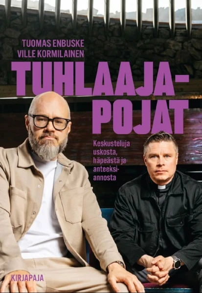Tuhlaajapojat -kirjan kansi. Vasemmalla parrakas Tuomas Enbuske hiekan värisessä asussa, oikealla Ville Kormilainen mustassa takissa liperit kaulassa.